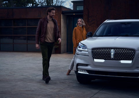A man and a woman approaching a 2024 Lincoln Aviator® SUV, which illuminates certain lights when they are close | Stivers Lincoln in Waukee IA