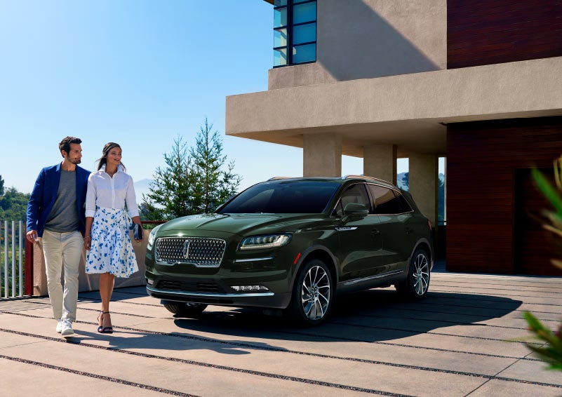 A couple walk away from a 2023 Lincoln Nautilus® SUV parked in the driveway of a hillside home.