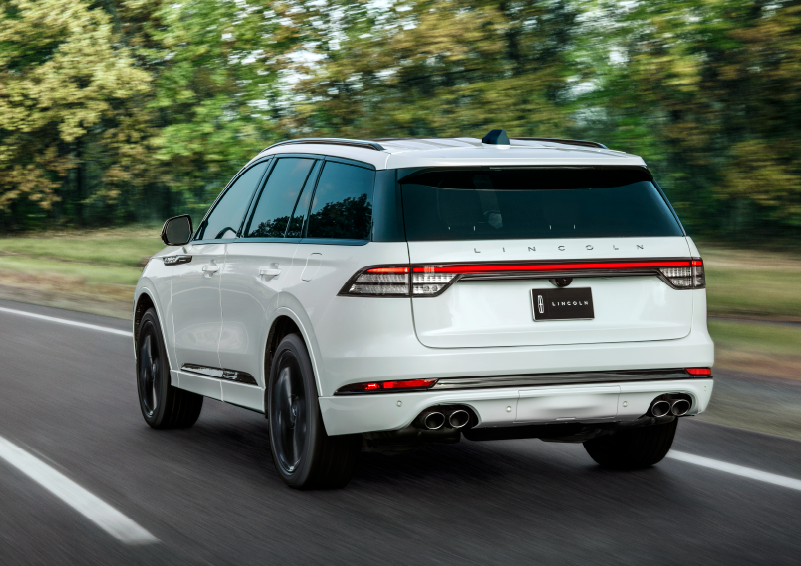 A white 2025 Lincoln Aviator® SUV is being driven away down a road lined with colorful trees. | Stivers Lincoln in Waukee IA