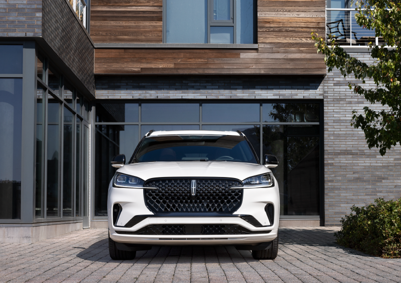 A white 2025 Lincoln Aviator® SUV is shown parked outside a modern building with gray brick and wood accents. | Stivers Lincoln in Waukee IA