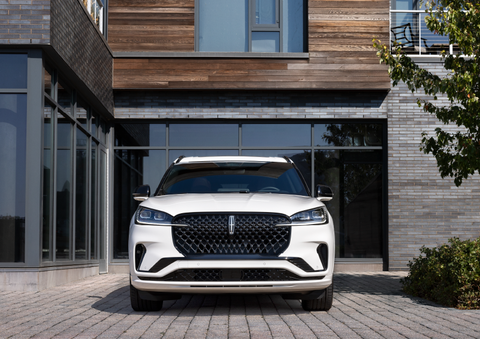 A white 2025 Lincoln Aviator® SUV is shown parked outside a modern building with gray brick and wood accents. | Stivers Lincoln in Waukee IA