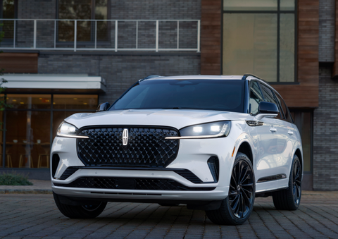 A white 2025 Lincoln Aviator® SUV is shown parked outside a modern building with gray brick and wood accents. | Stivers Lincoln in Waukee IA