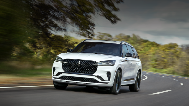 A white 2025 Lincoln Aviator® SUV is being driven down a road lined with trees. | Stivers Lincoln in Waukee IA