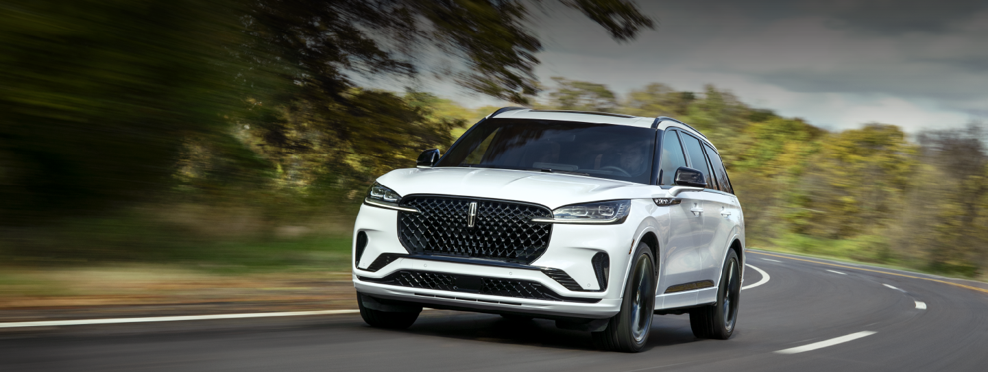 A white 2025 Lincoln Aviator® SUV is being driven down a road lined with trees. | Stivers Lincoln in Waukee IA