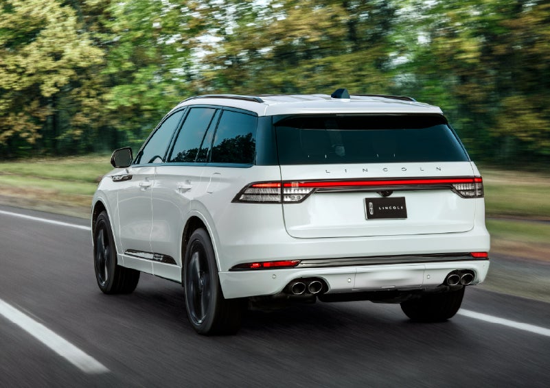A white 2026 Lincoln Aviator® SUV is being driven away down a road lined with colorful trees. | Stivers Lincoln in Waukee IA