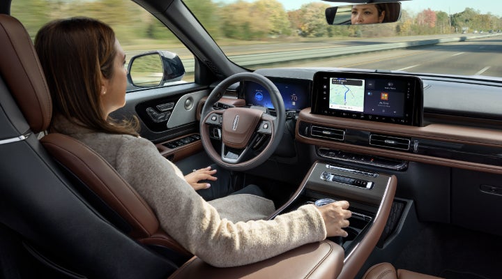 A 2026 Lincoln Aviator® SUV is being driven hands-free on a highway near a forest | Stivers Lincoln in Waukee IA