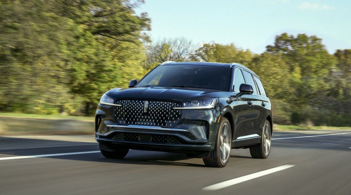 A 2026 Lincoln Black Label™ Aviator® SUV is being driven down a road lined with trees. | Stivers Lincoln in Waukee IA