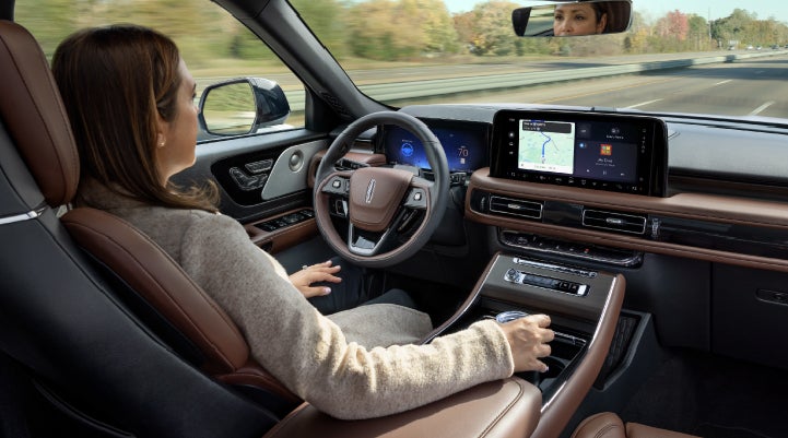 A 2027 Lincoln Aviator® SUV is being driven hands-free on a highway lined with trees. | Stivers Lincoln in Waukee IA