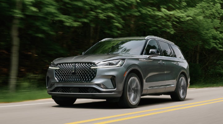 A 2027 Lincoln Aviator® SUV is being driven down a road lined with trees. | Stivers Lincoln in Waukee IA